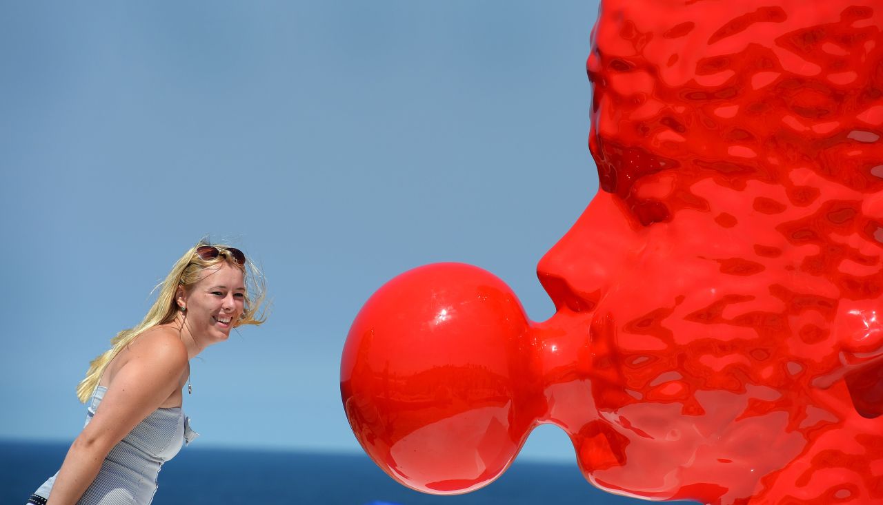 Una turista observa una escultura de dos metros de color rojo sangre y cuya cabeza  sopla un chicle. Su autor es  Qian Sihua y esta instalada en el paseo Tamarama, en  la costa de Sydney, Australia.  Es la mayor exposición de esculturas al aire libre del mundo y cuenta con más de 100 esculturas de artistas internacionales. (AFP / WILLIAM WEST) 