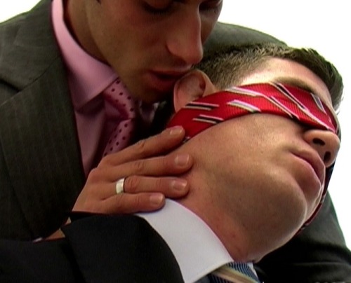 A man in a suit is blindfolded with his tie as another man also dressed in a suit holds the back of his head and leans down to place his mouth near the blindfolded man&#8217;s ear.
This is a fantastic photograph for all the reasons soft-core erotica can be sexy: the narrative exposed by the picture rather than the visual stimulus of the image itself. This picture is great in all the ways artsy-fartsy photographs are not. (And look, no monochrome necessary!)
Another noteworthy point in this image is the use of the man&#8217;s suit tie as a blindfold. I own three ties, and though I ostensibly purchased them for work I would much rather use them as sex toys. Many facets of menswear can be extremely useful bondage, ties and belts chief among them.
-maymay
derekisme:
well dressed lovers