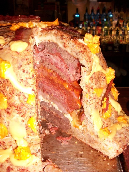 Meta Meat Cake Four types of sausage, bratwurst, chorizo, ground beef, ground pork, diced ham, Canadian bacon, pepperoni, hickory smoked bacon, hot cappy, queso blanco, provolone and sharp cheddar, wrapped in sausage, bacon and cheese ball dough and baked. Then decorated with American, cheddar squeeze cheese and bacon strips. (submitted by Mason Von Rouge)  