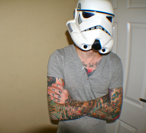 A man with a Storm Trooper mask on and multiple tattoos on his chest and 