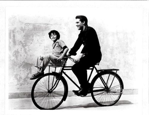 Elvis Presley and Larry Domasin ride a bike.