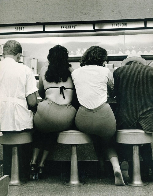 Two women share a stool at the diner, 1950s.